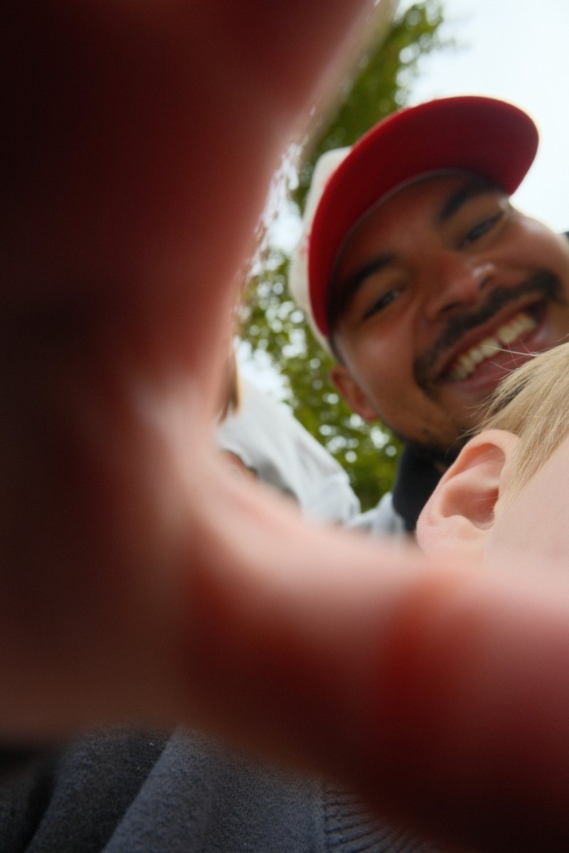 AJ Harris laughing in a red cap, shot from below past a hand blurred across the foreground